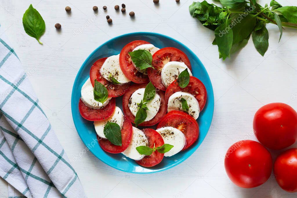 traditional Italian caprese salad on the blue plate. sliced red tomatoes, mozzarella cheese, green basil, olive oil on a white background. fresh salad with copy space. top view.flat lay