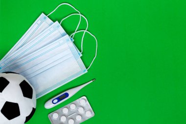Futbol arka planı. Futbol ya da futbol topunun tıbbi maskeli hali, yeşil arka planda haplar. Covid-19 veya Coronavirus ile spor müsabakaları konsepti. Boşluğu kopyala