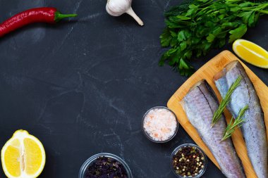 Çiğ pollock balığı. Ahşap kesme tahtasında pişmemiş pollock ve siyah taş masada pişirmek için malzemeler. Limon, tuz ve biberli taze deniz ürünleri. Kopyalama alanı olan üst görünüm.