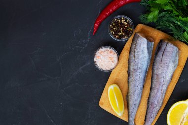 Taze pollock balığı. Ahşap kesme tahtasında pişmemiş pollock ve siyah taş masada pişirmek için malzemeler. Limon, tuz ve biberli çiğ deniz ürünleri. Kopyalama alanı olan üst görünüm.