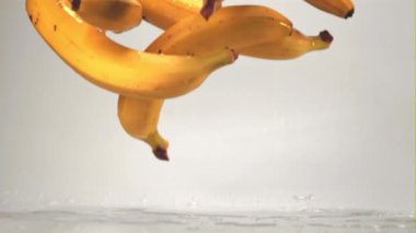 Beyaz arka planda süper yavaş çekimde muzlar sıçramalı bir masaya düşerler. 1000 fps hızla yüksek hızlı bir kamerayla çekildi..