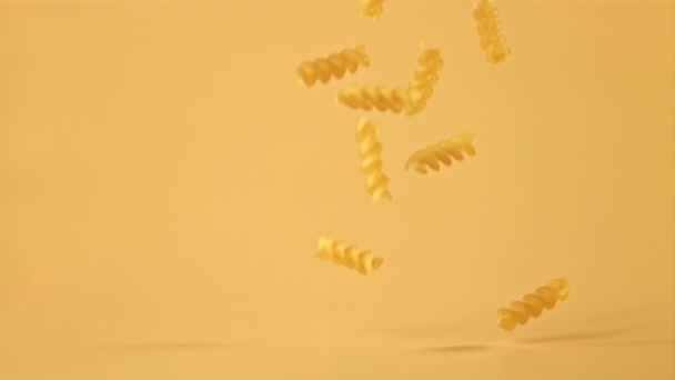 Kuru fusilli makarna süper yavaş çekimde turuncu arka plana düşer. 1000 fps hızla yüksek hızlı kamera ile çekilir.. — Stok video