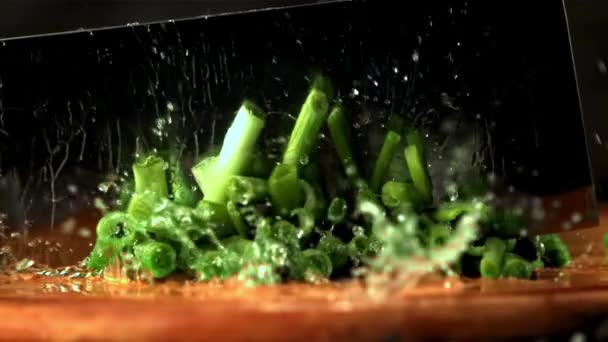 Super slow motion stukjes groene ui afgesneden met een groot mes. Gefilmd met 1000 fps. — Stockvideo