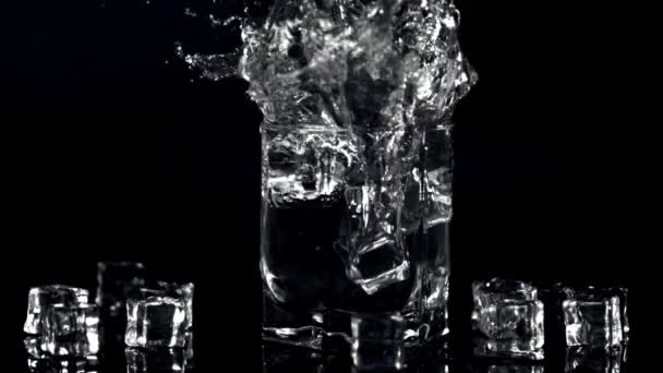 Super slow motion isbitar faller i ett glas vatten med spray. Inspelning vid 1000 fps. — Stockvideo