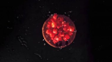 Süper yavaş çekimde, ahşap bir tabakta, üzerinde su damlaları olan kırmızı biber parçaları. 1000 fps hızla yüksek hızlı bir kamerayla çekildi..