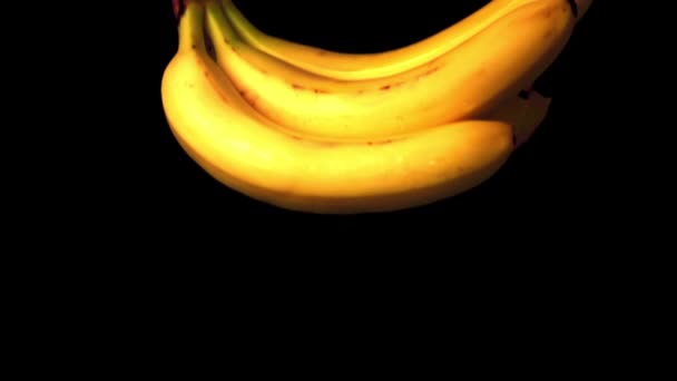 Сверхмедленное движение: на стол падает куча бананов на чёрном фоне.. — стоковое видео