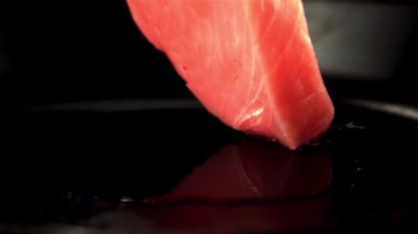 Süper yavaş çekimde çiğ ton balığı bifteği bir parça yağlı tavaya düşer. 1000 fps hızla yüksek hızlı bir kamerayla çekildi..