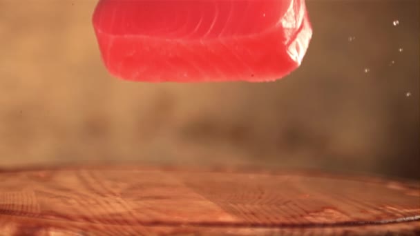 Filete de atún fresco en cámara súper lenta cae sobre una tabla de cortar con salpicaduras de agua. Filmado en una cámara de alta velocidad a 1000 fps. — Vídeo de stock