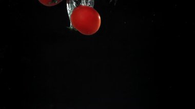 Siyah arka planda suyun altına düşen taze domatesler. 1000 fps 'de yüksek hızlı bir kamerayla çekildi. Yüksek kaliteli FullHD görüntüler