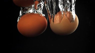 Siyah arka planda suyun altına düşen yumurtalar. 1000 fps 'de yüksek hızlı bir kamerayla çekildi. Yüksek kaliteli FullHD görüntüler