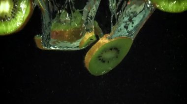 Dilimlenmiş kivi siyah arka planda suyun altına düşüyor. 1000 fps 'de yüksek hızlı bir kamerayla çekildi. Yüksek kaliteli FullHD görüntüler