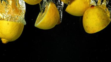 Limon dilimleri siyah arka planda suyun altına düşüyor. 1000 fps 'de yüksek hızlı bir kamerayla çekildi. Yüksek kaliteli FullHD görüntüler