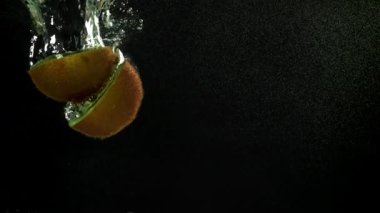 Dilimlenmiş kivi siyah arka planda suyun altına düşüyor. 1000 fps 'de yüksek hızlı bir kamerayla çekildi. Yüksek kaliteli FullHD görüntüler