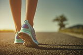 Closeup běžkyně oholené nohy v běžecké boty pro běh na silnici při východu nebo západu slunce