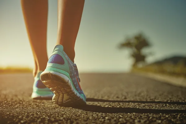 Fechar-se do corredor feminino raspado pés em tênis de corrida indo para uma corrida na estrada ao nascer do sol ou pôr do sol — Fotografia de Stock