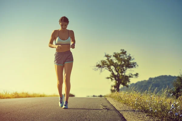 Vacker vältränad kvinna i sport shorts kör på en väg på soluppgång eller solnedgång — Stockfoto