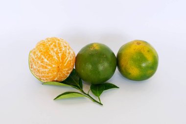 Beyaz arka planda yeşil yapraklı yeşil mandalinalar, biri soyulmuş.