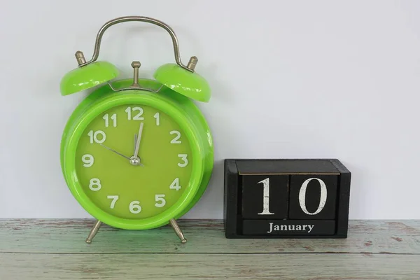 green alarm clock and cube calendar with January month on the table