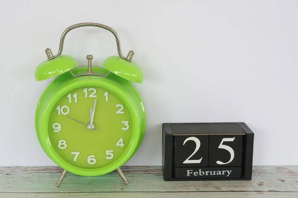 green alarm clock and cube calendar date with February month concept.
