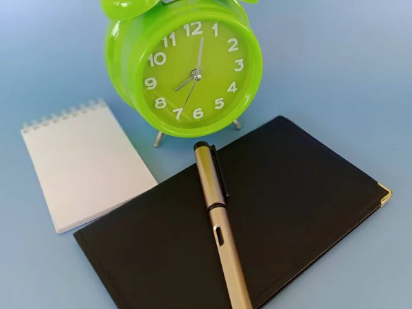 green alarm clock and pen on the desk
