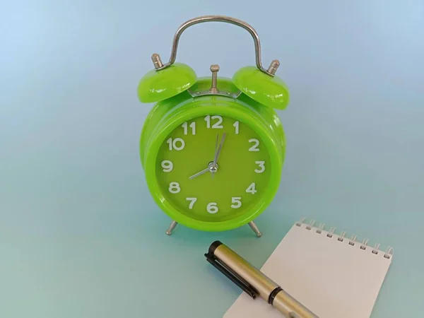 green alarm clock and pen on the desk