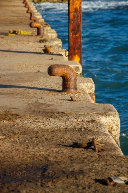 Balıkçı teknelerini bağlamak için kullanılan demirlerle betondan yapılmış rıhtımın soyut bir görüntüsü var. Metal paslanmış ve deniz suyuyla aşınmış.