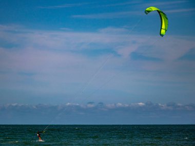Bir paraşüt sörfçüsü gökyüzü arka planına sahip bir paradisial denizde bazı dalgalar sürüyor.