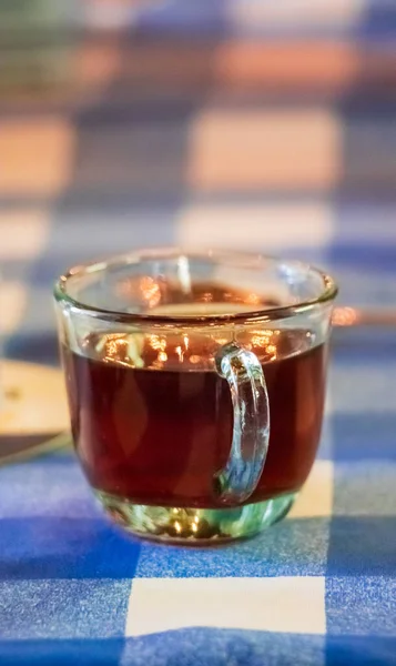 A hot delicious cup of tea on a transparent cup over a table with a blue and white tablecloth