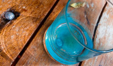 Kırsal bir ahşap masadaki su bardağının aşırı detayı bazı nedenseller ve gölgeler yaratıyor.