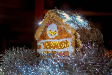Karla kaplı ev yapımı zencefilli kurabiye evi ve karanlık arka planda Noel ışıkları.