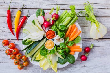 Beyaz tabakta farklı soslar ve ahşap arka planda taze çiğ sebzeler..