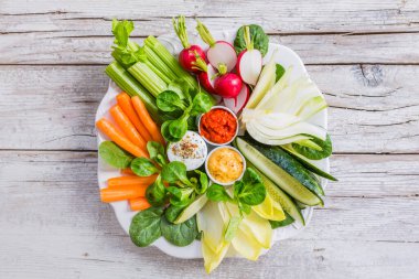 Beyaz tabakta farklı soslar ve ahşap arka planda taze çiğ sebzeler. Vejetaryen diyeti. Sağlıklı Yeme.