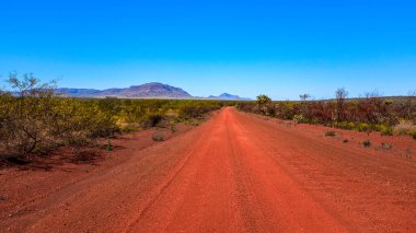 Karijini Ulusal Parkı 'nda çarpıcı bir kırsal alan, engebeli geçitleri, kızıl kaya oluşumlarını ve geniş kurak arazileri gözler önüne serer. Sahne, Batı Avustralya 'nın ham doğal güzelliğini, jeolojik özelliklerini ve ıssız çöllerini vurguluyor..