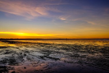 Güneş, Port Hedland sahil şeridinde batıyor. Sıcak renkler gökyüzüne saçılıyor ve alçak gelgitte ıslak kuma yansıyor. Bu sakin sahne engebeli güzelliği, engin kıyı şeridini ve kuzey batı Avustralya 'nın sakin atmosferini yakalar..