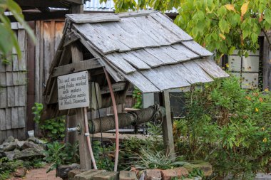 Kırsal bir kereste dilek kuyusu ve testere, eskimiş ve yıpranmış, bir miras bahçesinde yemyeşil bir yerde oturuyor. Sahne nostalji ve çekiciliği çağrıştırıyor, geleneksel zanaatkarlığı ve tarihsel bahçenin ebedi güzelliğini vurguluyor..