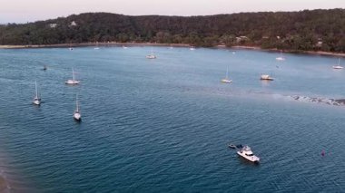 Smooth aerial footage gliding over moored boats resting in the calm bay at Seventeen Seventy (1770). The view leads toward the shoreline and popular campground, capturing serene waters, coastal scenery, and the relaxed Queensland holiday atmosphere.