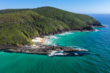Forster 'daki Seven Mile Plajı' nda Janies Corner 'ı çeken hava görüntüsü geniş bir kumla buluşan okyanus dalgalarını gösteriyor. Yükseltilmiş perspektif kıyı dokularını, sörf hatlarını ve berrak mavi suyu vurgular ve manzaralı bir deniz manzarası yaratır..