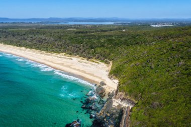 Forster 'daki Seven Mile Plajı' nda Janies Corner 'ı çeken hava görüntüsü geniş bir kumla buluşan okyanus dalgalarını gösteriyor. Yükseltilmiş perspektif kıyı dokularını, sörf hatlarını ve berrak mavi suyu vurgular ve manzaralı bir deniz manzarası yaratır..