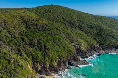 Forster 'daki Seven Mile Plajı' nda Janies Corner 'ı çeken hava görüntüsü geniş bir kumla buluşan okyanus dalgalarını gösteriyor. Yükseltilmiş perspektif kıyı dokularını, sörf hatlarını ve berrak mavi suyu vurgular ve manzaralı bir deniz manzarası yaratır..