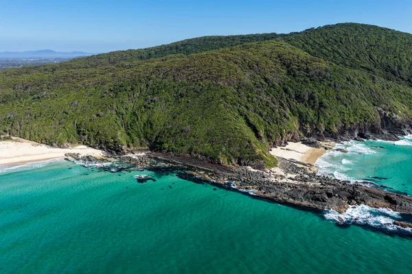 Forster 'daki Seven Mile Plajı' nda Janies Corner 'ı çeken hava görüntüsü geniş bir kumla buluşan okyanus dalgalarını gösteriyor. Yükseltilmiş perspektif kıyı dokularını, sörf hatlarını ve berrak mavi suyu vurgular ve manzaralı bir deniz manzarası yaratır..