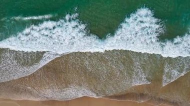 Hava aracı, Forster 'daki Seven Mile Plajı' ndaki kumlu bir sahil şeridinde dalgalarla birlikte turkuaz okyanus suyunu aşağı doğru görüyor. Üst alt perspektif, sahil boyunca doğal kıyı şekillerini ve temiz suyu vurgular..