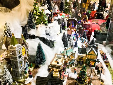 Yeni yıl manzarası. Vitrin için minyatür. Üç köşeli çatıları olan küçük evler ve merkezde oyuncak insanlar. Merkezinde büyük bir analog saati olan bir kilise var..