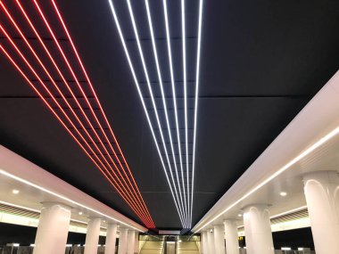 Tavanda parlak LED şeritler var. Mavi ve beyaz çizgiler, aydınlatma. Metrodaki tavanın süslemesi. Beyaz, kalın kolonların etrafında....