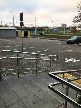 Veranda, kamu binasından otoparka giriş izni. Engelli insanların oturduğu geniş bir otopark. Şafakta yürüyün. Siyah metal parmaklıklar. Otobüs durağı ve çöp kutularının yanına park et..