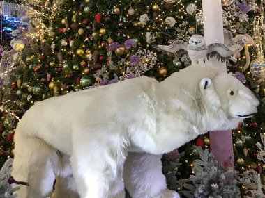 Noel süslemeleri. Oyuncak bir kutup ayısı, toplar, çelenkler ve yağmurla süslenmiş yapay bir Noel ağacının yanında duruyor. Noel arifesi. Ziyaretçiler için stilize sergi.
