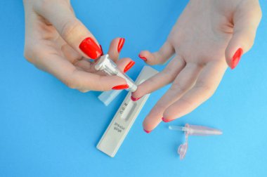 Bir mızrakla parmağın delinmesi. Hızlı kan testi. Koronavirüs teşhisi için test şeridi. Kırmızı manikürlü bir kız IgG ve IgM sınıfı antikorları tespit etmek için parmak izi ve iğne yapar..