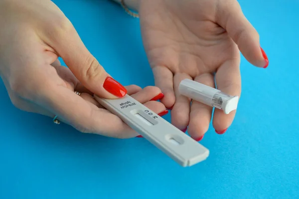 a girl with a bright red manicure holds a coronavirus test in her hand. a lancet for a blood test is nearby. determination of antibodies. detection of antibodies for immunity from coronavirus.