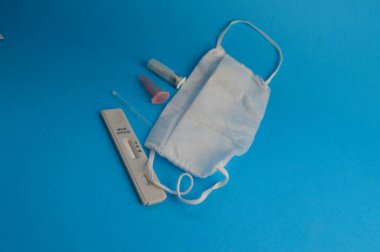 antikor testi. Mavi arka planda kendine koronavirüs enfeksiyonu teşhisi için bir şerit. Testin yanında, tek kullanımlık bir maske, bir neşter ve kan kabı analizi için bir pipet..