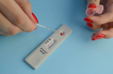 Mavi arka planda koronavirüs testi. Parlak kırmızı manikürlü kız kan testi yapıyor. IgG ve IgM antikorlarının belirlenmesi, hassas analiz.