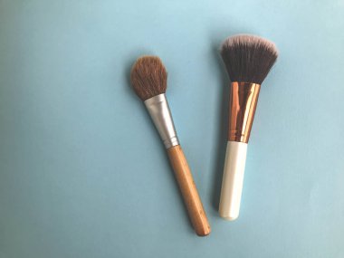 Güzel moda kozmetik güzellik göz alıcı beyaz ve altın fırçalar ve fırçalar makyaj, toz ve kozmetik ürünler sürmek için mavi, nazik bir arka planda. Düz yatıyordu.